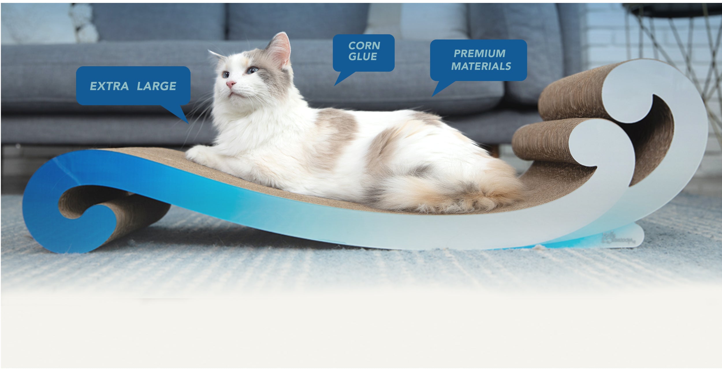 A cat reclines on a curved, blue and brown scratcher labeled "Extra Large," "Corn Glue," and "Premium Materials.