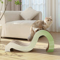 Load image into Gallery viewer, A fluffy cat is perched on a Mint Mint - Modern Cat Scratcher & Stretching Board made of premium cardboard in a softly curved design, situated in a brightly lit living room with a beige couch and potted plant in the background.
