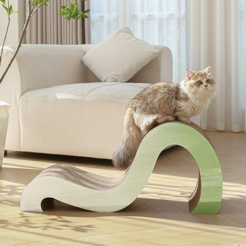 A fluffy cat is perched on a Mint Mint - Modern Cat Scratcher & Stretching Board made of premium cardboard in a softly curved design, situated in a brightly lit living room with a beige couch and potted plant in the background.